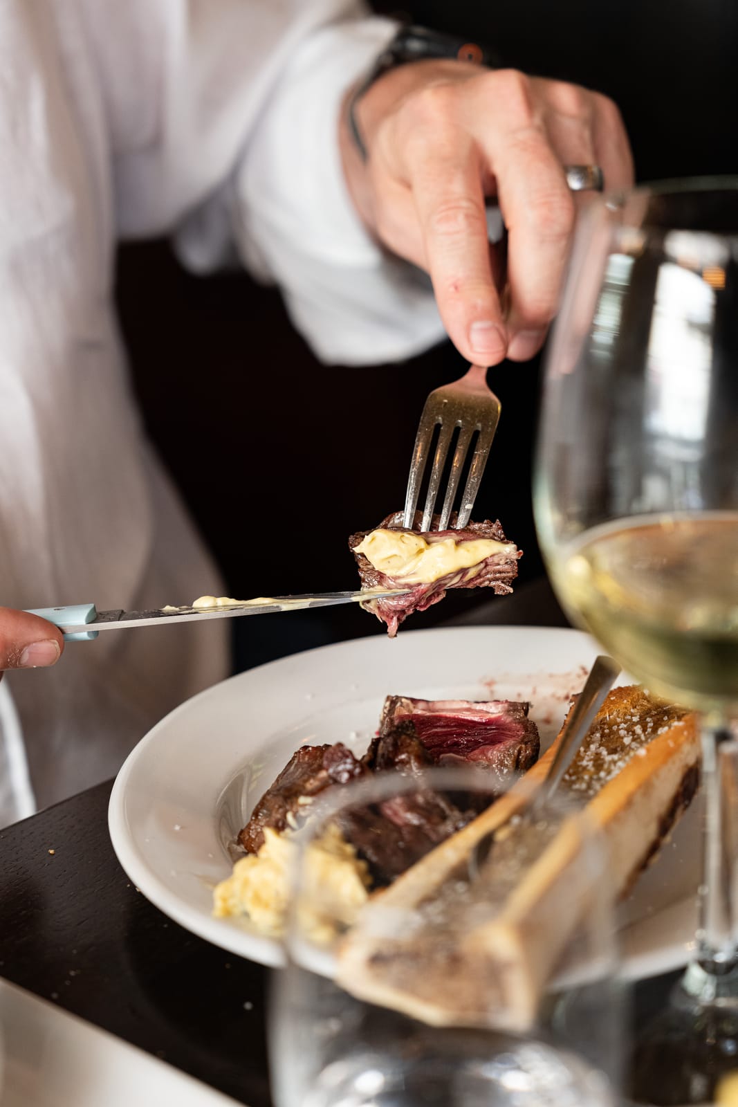 Un convive déguste un morceau de côte de bœuf avec de la sauce, un os à moelle dans l'assiette, chez À Côté