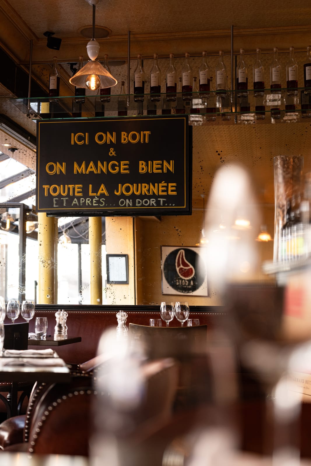 Salle d'À Côté avec banquettes, tables dressées et ardoise « Ici on boit et on mange bien toute la journée »
