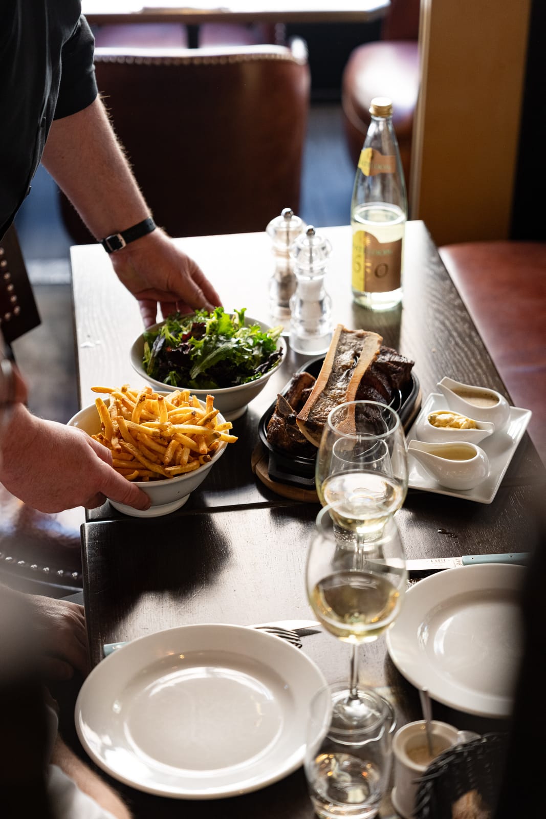 Una costata servita con osso con midollo, patatine fritte fatte in casa, insalata e salse al tavolo di À Côté