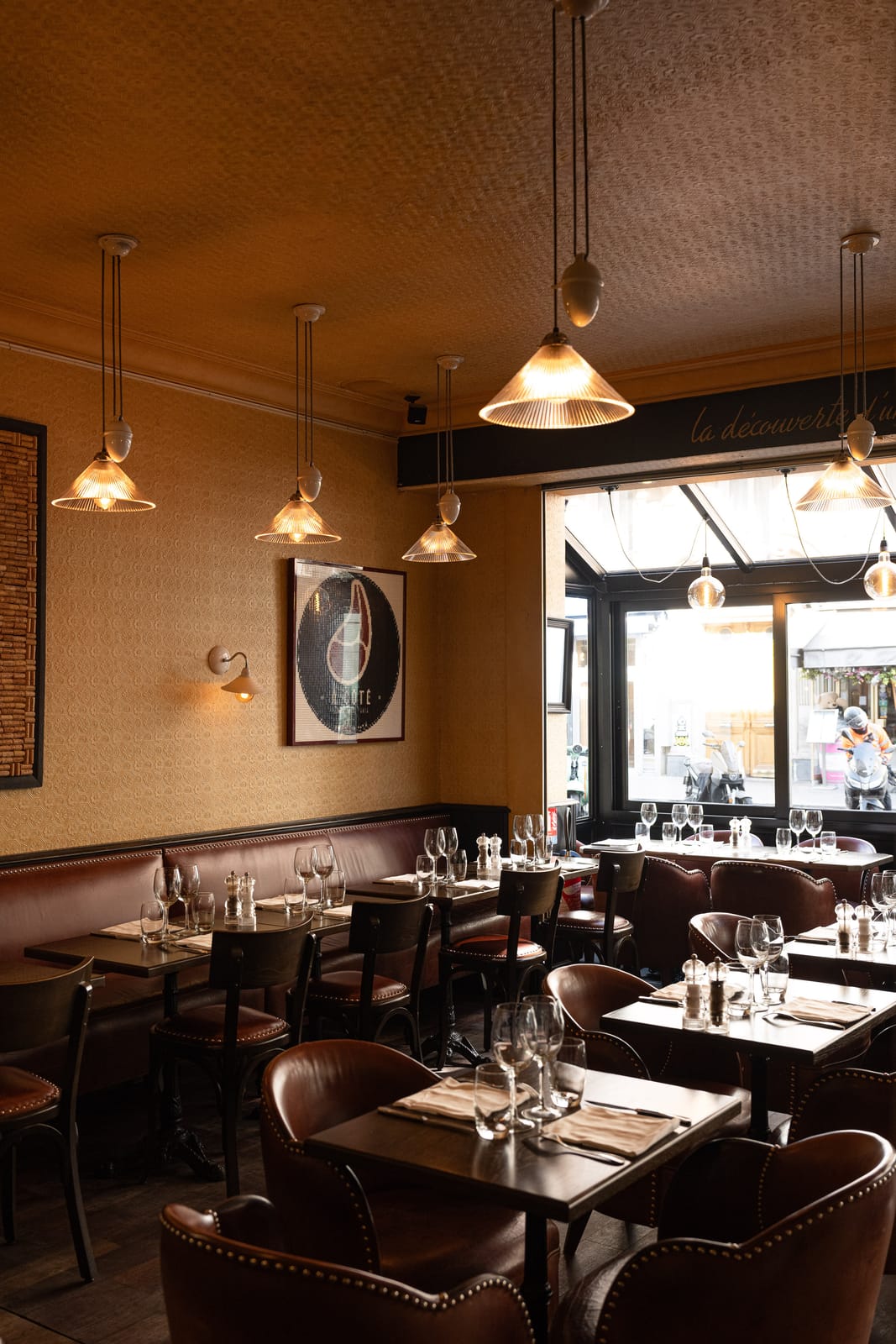 The dining room at À Côté: leather banquettes, laid tables and glass pendant lights, with the window onto the street