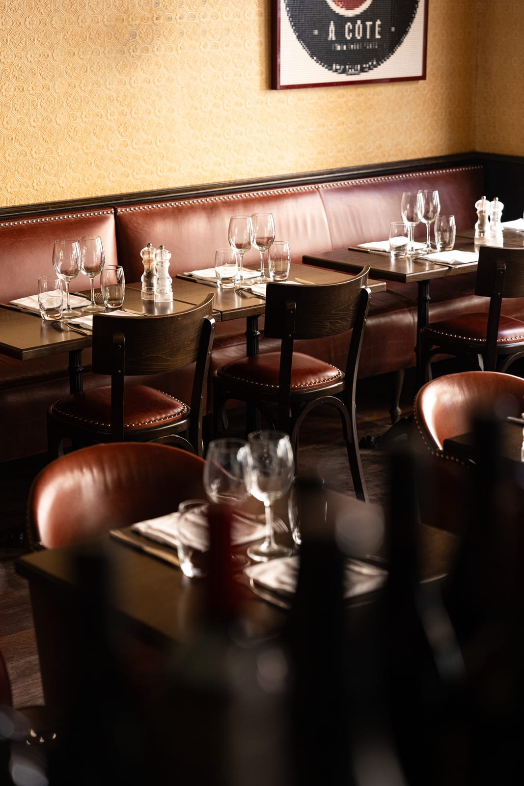 Tables dressées, banquette en cuir et chaises en bois dans la salle du restaurant À Côté