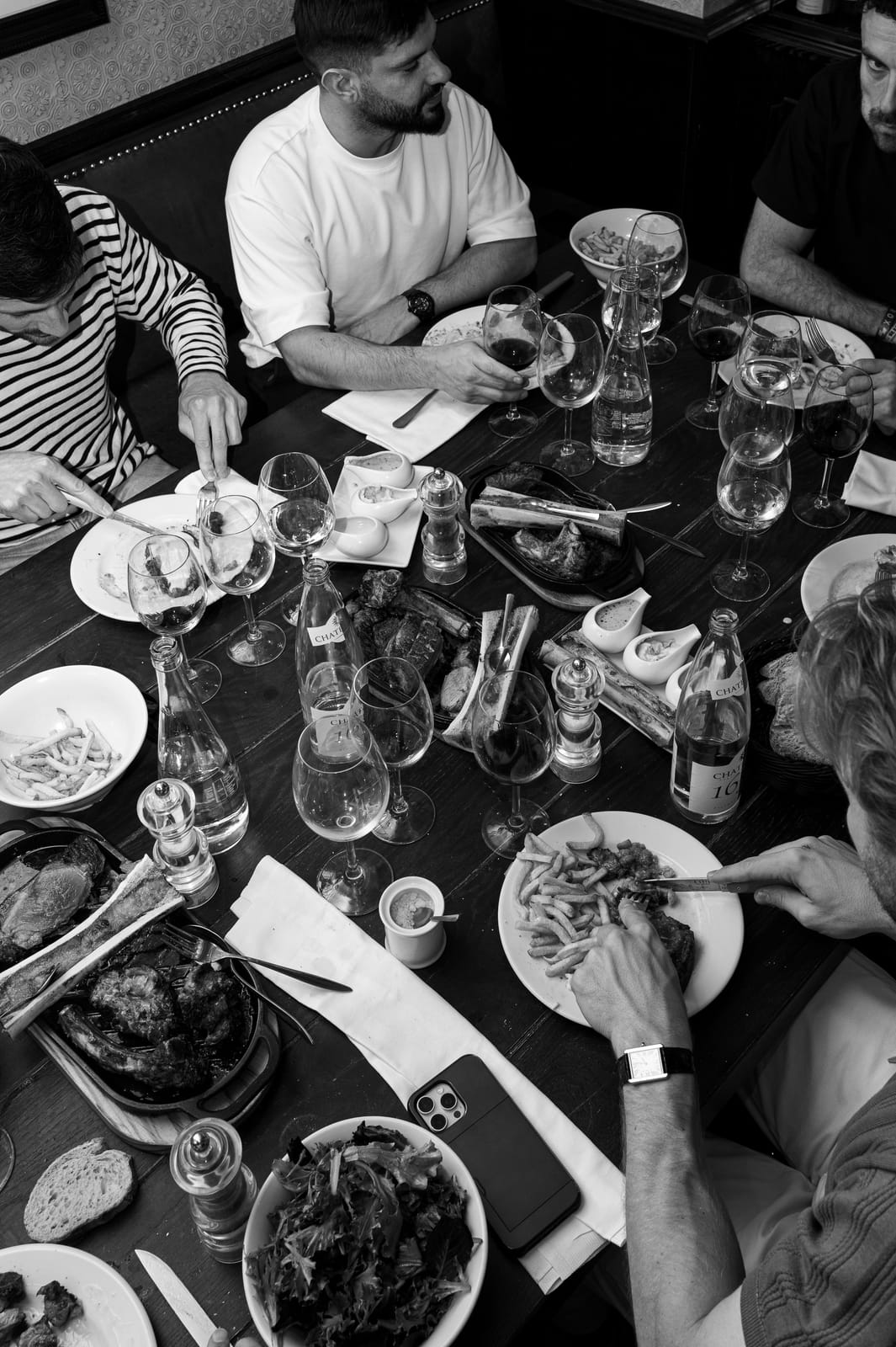 Commensali che condividono costate di manzo, patatine e vino a un tavolo di À Côté