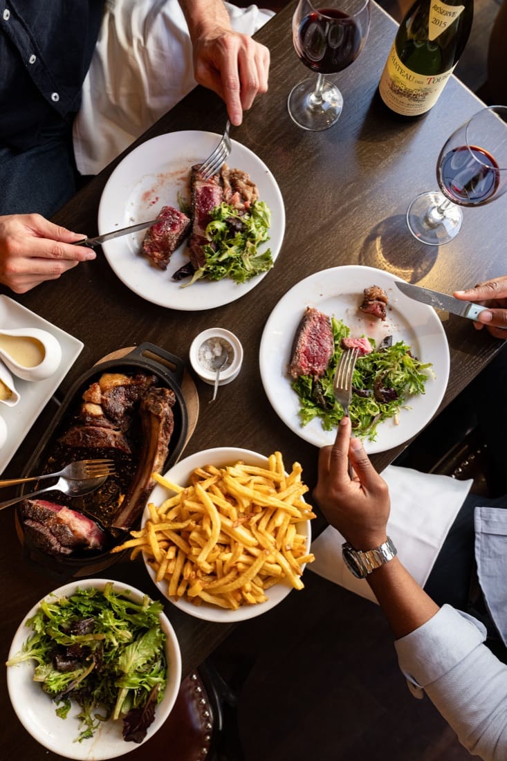 Table dressée : côte de bœuf, frites et salade à partager